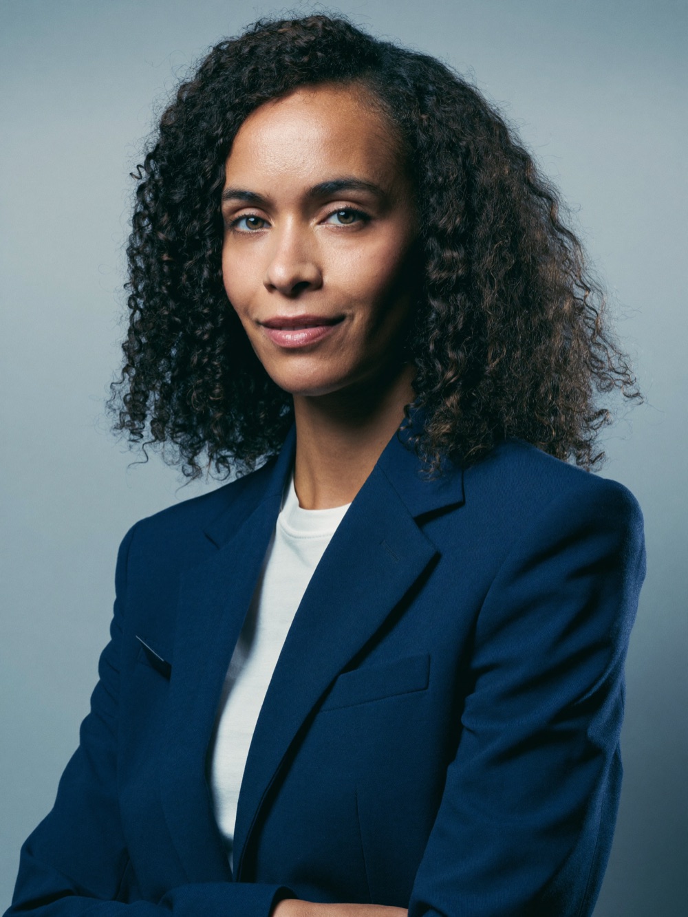 Nia, the studio's AI-generated digital attaché — a composed portrait of a woman in a navy blazer. She is not a real person.